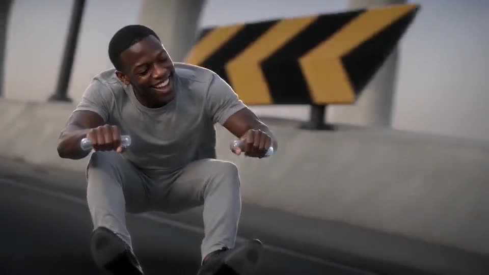 Still from the template: a smiling young man in a grey T-shirt hunched in mid-air, both fists forward on little grips, with a yellow-and-black warning board and an elevated highway behind him